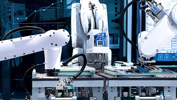 Drei weiße Roboterarme bearbeiten Werkstücke 