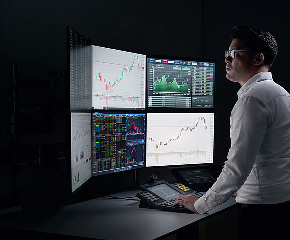 [Translate to English:] Mann stehend an Trading Arbeitsplatz mit mehreren Bildschirmen