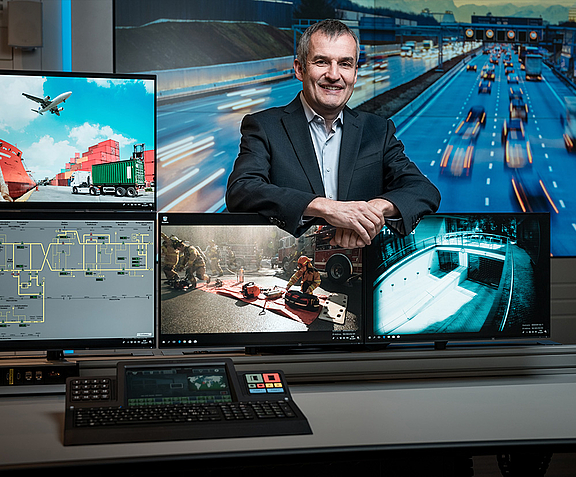 Mann im Anzug steht zwischen Bildschirmen und Video Walls im Control Room