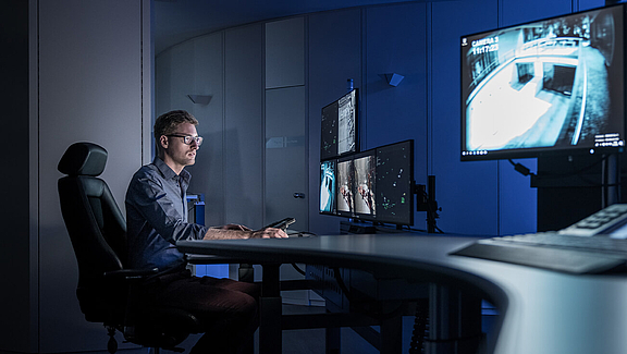 Mann sitzend im Control Room vor Bildschirmen und Video Wall