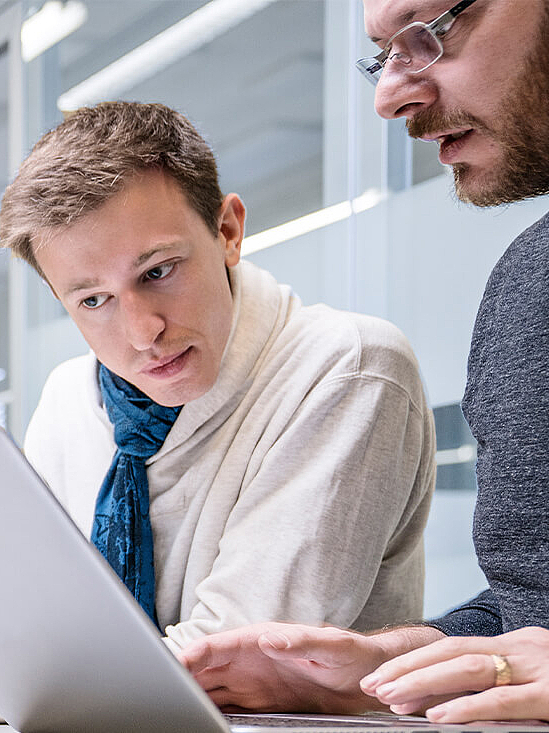 Zwei Männer an einem Laptop in Büroumgebung 