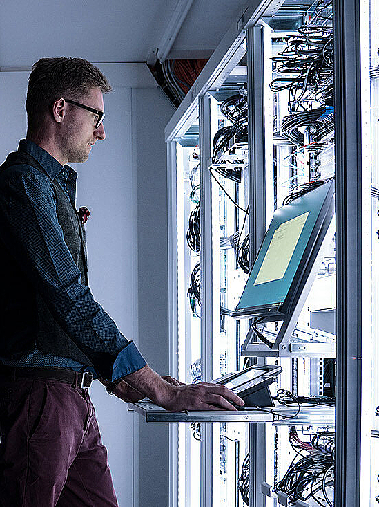 Mann in beleuchtetem Serverraum an einem Kontroll-Terminal