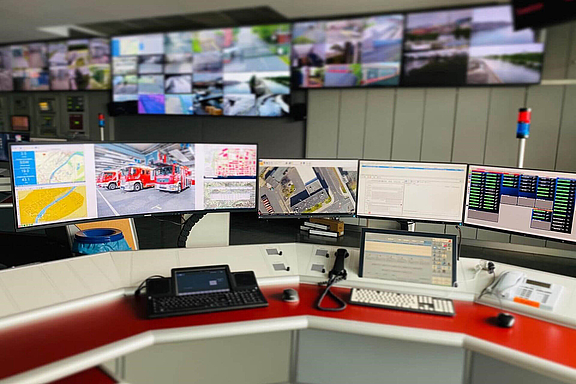 Control Room Arbeitsplatz mit mehreren Bildschirmen, Tastaturen und Video Walls im Hintergrund